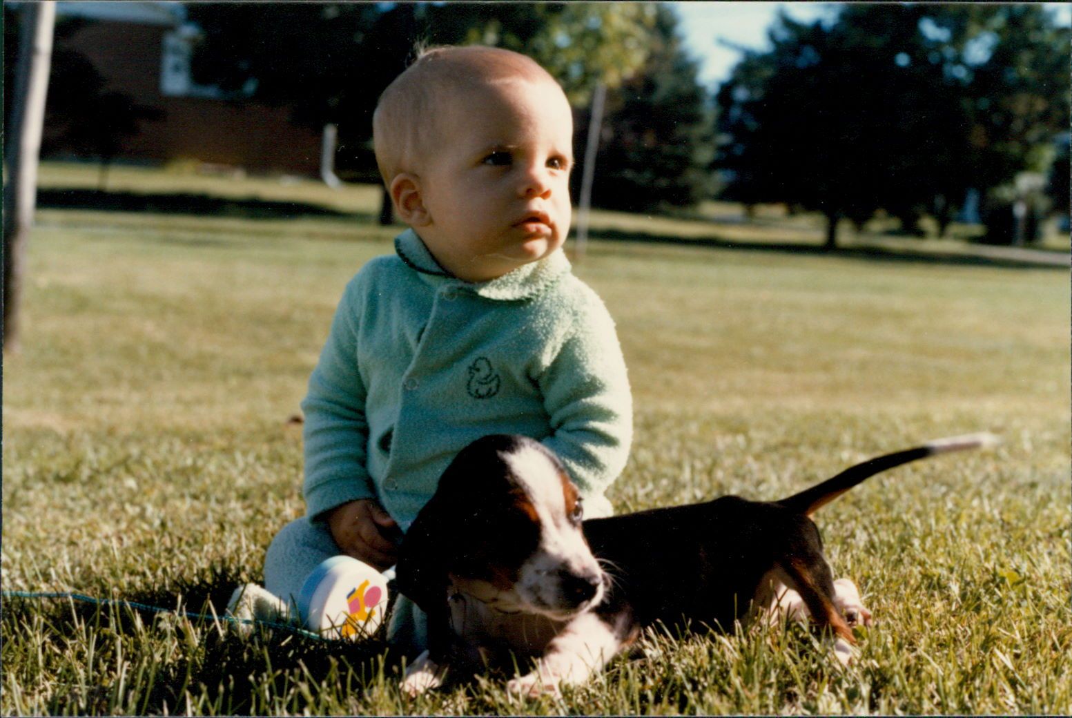 A baby and a puppy sitting outside in the lawn, with a vintage style