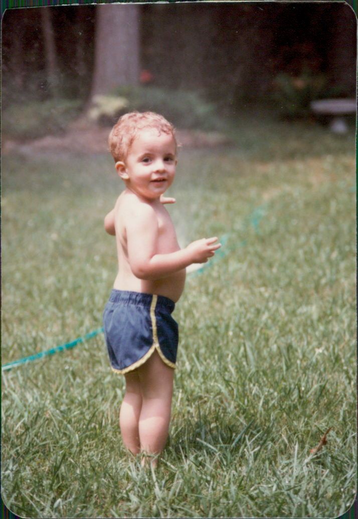 A young boy outside, holding a garden hose