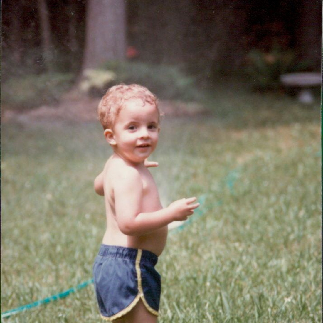 A young boy outside, holding a garden hose