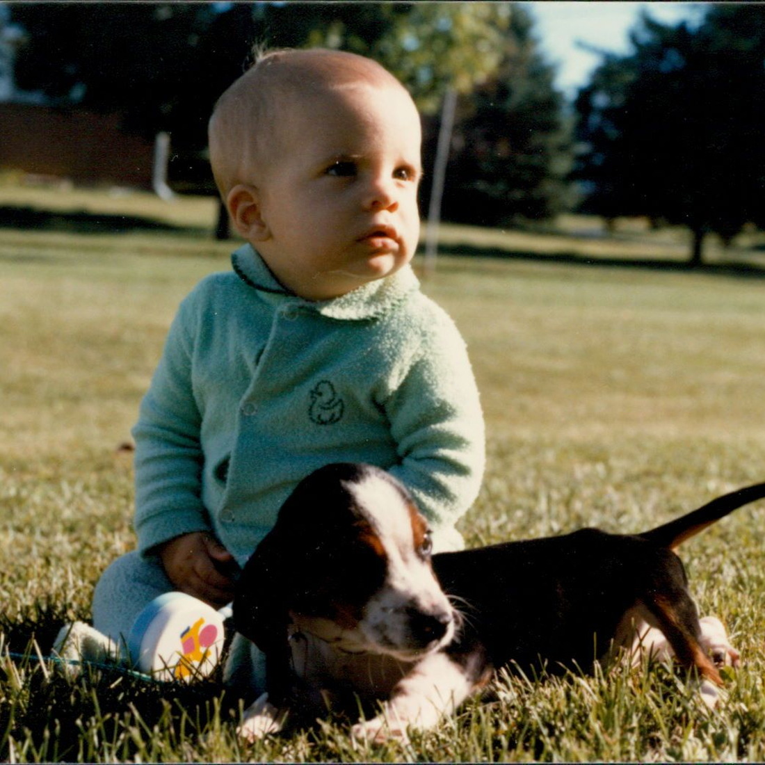 A baby and a puppy sitting outside in the lawn, with a vintage style