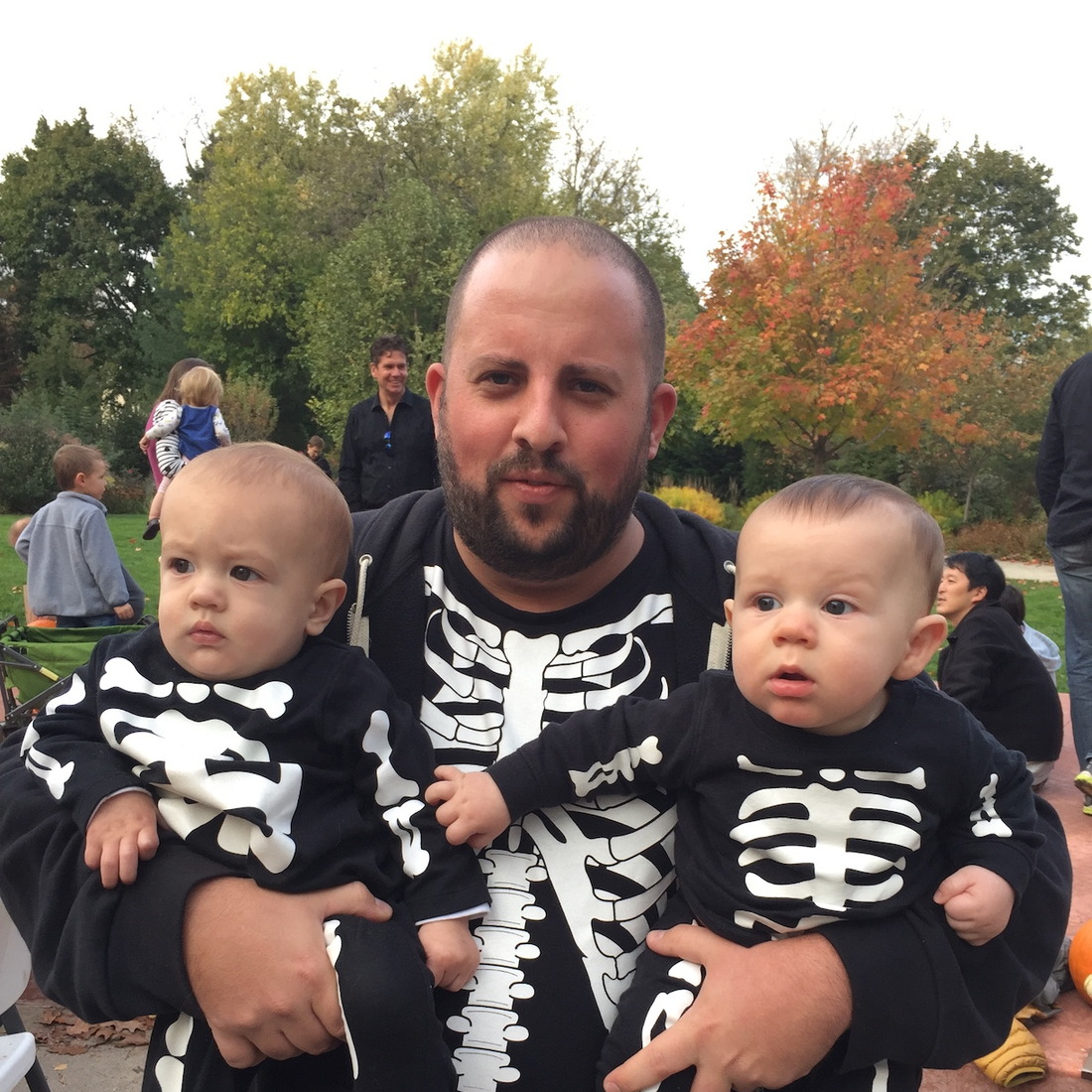 A man holding 2 babies, standing outside, all three wearing skeleton t-shirts